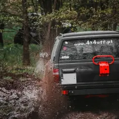 Czarny SUV pruje przez błoto, rozpryskując je na boki. To właśnie jest **cruising** w terenie, czyli jazda po bezdrożach.