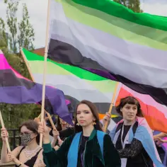 Osoby niosą tęczowe flagi, w tym flagę aromantyczności, podczas parady.