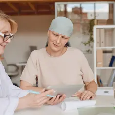 Lekarka omawia z pacjentką w chuście na głowie tablet, być może decyzję o rezygnacji z hormonoterapii.