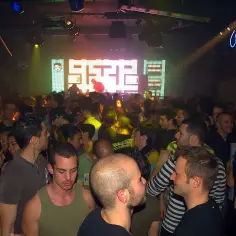 Tłum ludzi tańczy w klubie nocnym przy kolorowej, podświetlanej scenie.