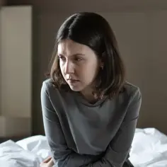 Młoda kobieta siedzi na łóżku, pogrążona w myślach. Szuka sposobu, jak wyjść z depresji, czując się przytłoczona.