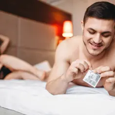 Mężczyzna otwiera prezerwatywę Durex. Kobieta w czarnej bieliźnie leży na łóżku.