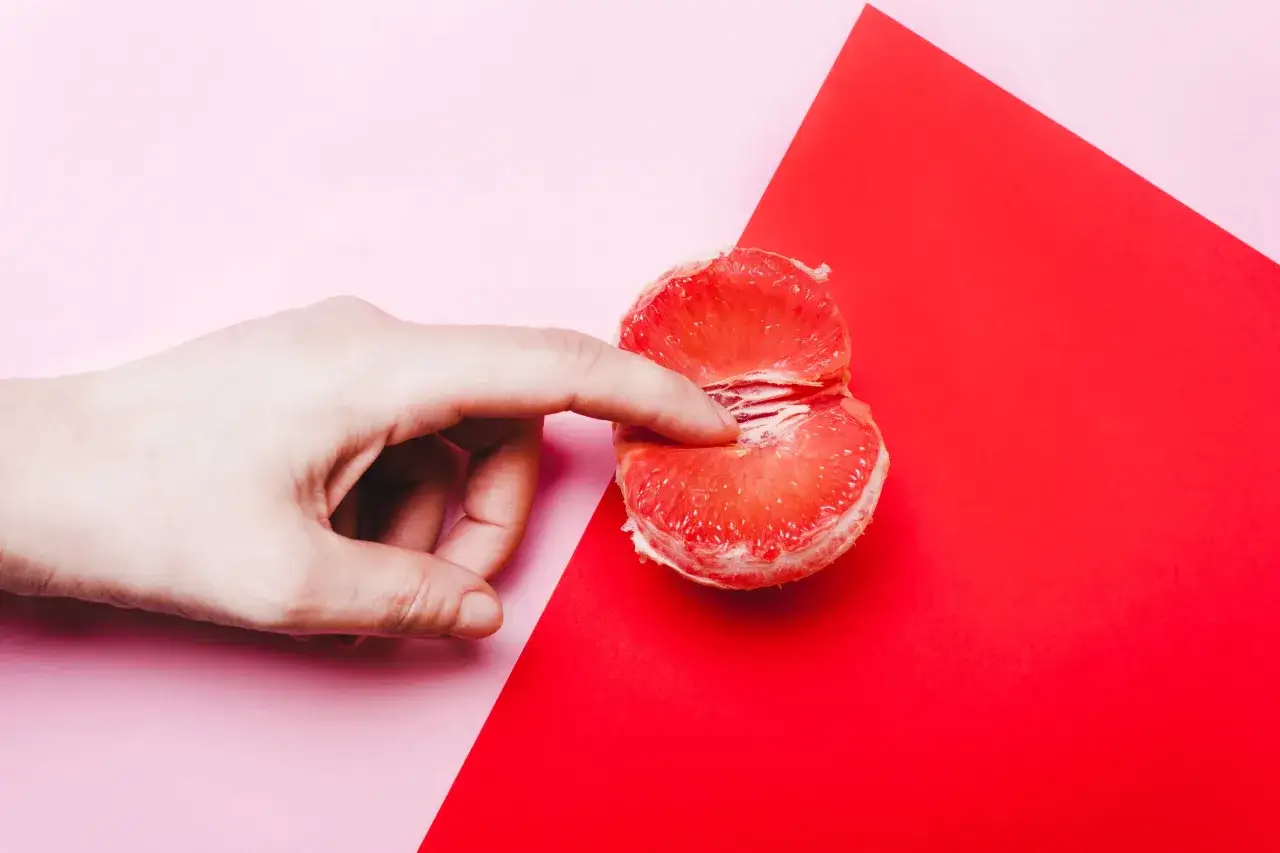 Dłoń delikatnie rozchyla kawałek grejpfruta, symbolizując różnorodne rodzaje pochwy u kobiet.